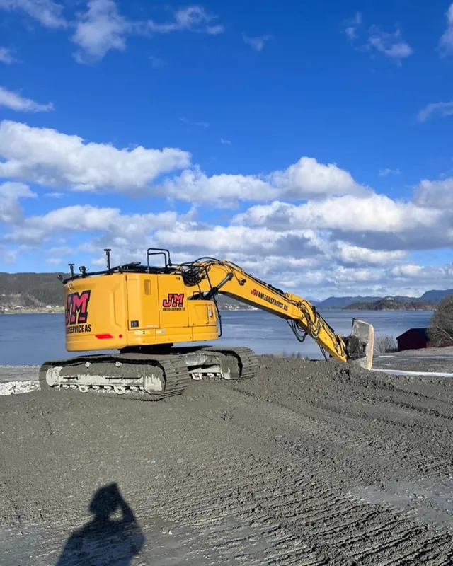 Gravemaskin på et planert grusområde ved sjøen