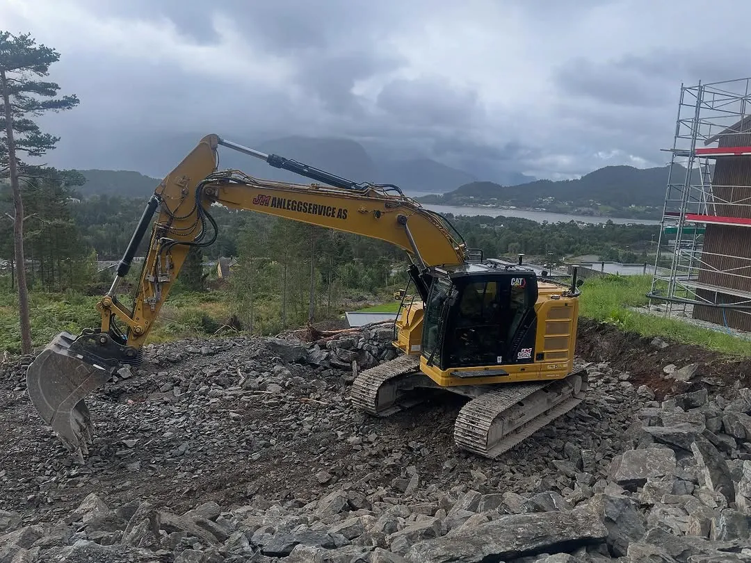 Gravemaskin på en ryddet tomt med fjord og fjell bak