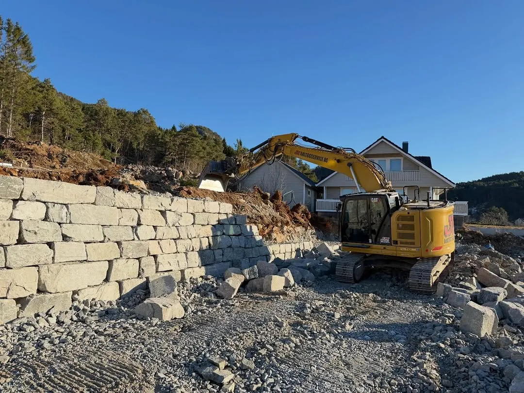 Gravemaskin ved en høy natursteinsmur