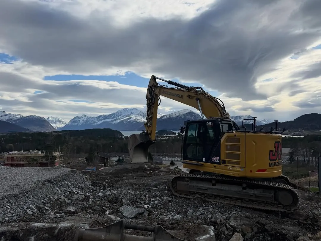 Gravemaskin på en byggeplass under snødekte fjell