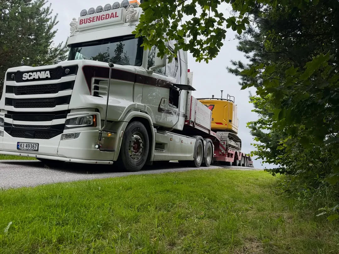 Gravemaskin på henger bak en lastebil, på vei til neste jobb